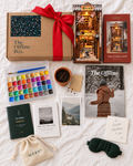 Everything in the MERRI Christmas Box laid out: the box tied with a red ribbon, the book nook, the pearl watercolour set, the magazine, the Passport, the Manuscript, seeds in a pot and a weighted eye mask