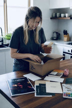 Someone unpacking an Offline Box at a kitchen bench, with the magazine, a book and a terracotta pot on the table