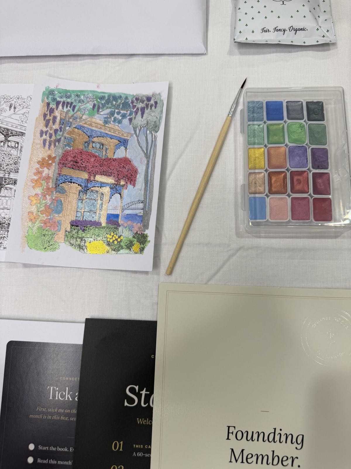The watercolour card, painted, beside the paint set