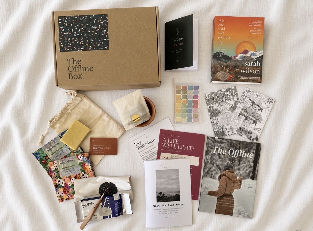Everything in a past Offline Box laid out on linen: a book, the magazine, watercolours, soap, beeswax wraps and the Manuscript